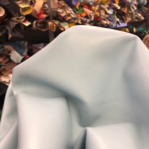 May include: A light blue leather hide, folded and draped over a surface. The leather has a smooth, soft texture.