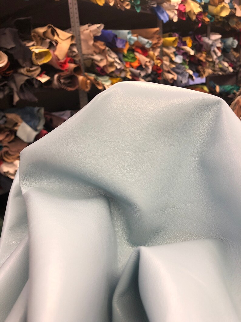 May include: A light blue leather hide, folded and draped over a surface. The leather has a smooth, soft texture.