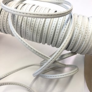 May include: White leather cord with a stitched edge. The cord is rolled up and ready to be used for crafting projects.