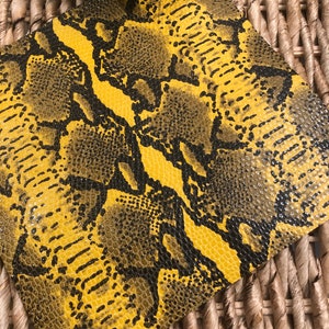 May include: Yellow and black snakeskin patterned fabric. The fabric has a textured surface and a repeating pattern of black and yellow scales.