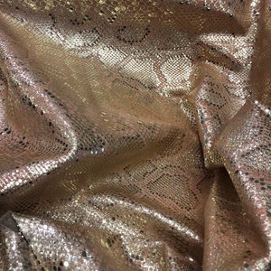 May include: Close-up of a gold and pink snakeskin fabric with a textured pattern.