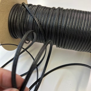 May include: A spool of black leather cord, wound around a cardboard core. The cord is smooth and has a subtle sheen.