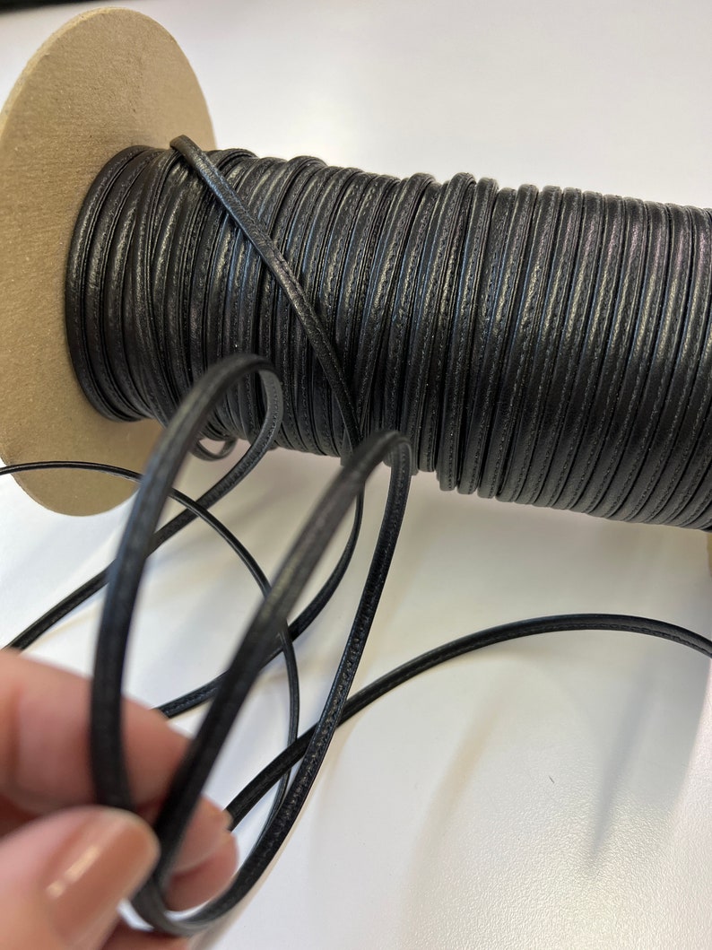 May include: A spool of black leather cord, wound around a cardboard core. The cord is smooth and has a subtle sheen.