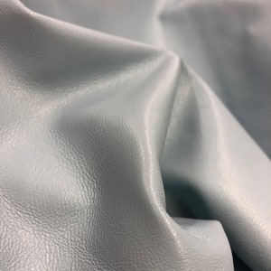 May include: A close-up of a light blue leather fabric with a textured surface.