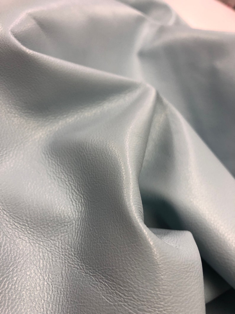 May include: A close-up of a light blue leather fabric with a textured surface.