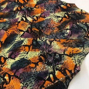 May include: A close-up of a fabric with a snakeskin pattern in shades of orange, purple, green, and black.