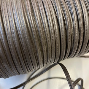 May include: A spool of brown leather cord with a stitched edge. The cord is wound tightly and is ready to be used for crafting projects.