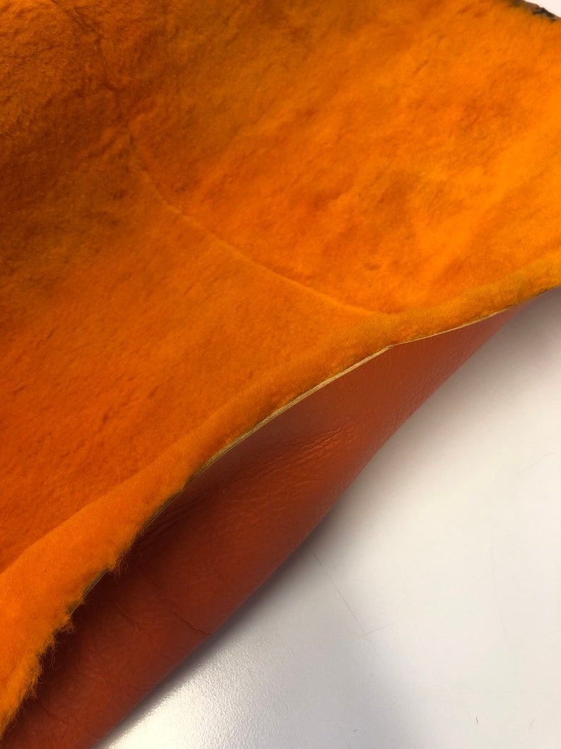 May include: A close-up of a piece of orange fabric with a fuzzy texture on one side and a smooth, brown leather texture on the other side.