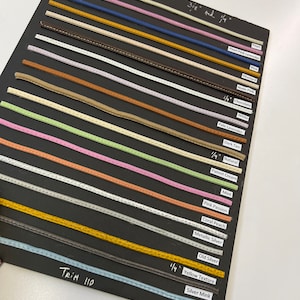 May include: A black card with a variety of colored leather trim samples. The trim samples are labeled with their color names and sizes, including 3/8 inch and 1/4 inch. The card is labeled "Trim 110".