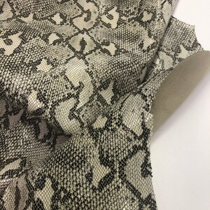 May include: Close-up of a white and black snakeskin fabric with a textured pattern. The fabric is folded and shows the texture of the material.