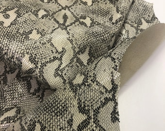 May include: Close-up of a white and black snakeskin fabric with a textured pattern. The fabric is folded and shows the texture of the material.