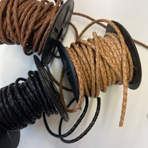 May include: Three spools of braided leather cord. One spool is black, one is brown, and one is a lighter brown color.