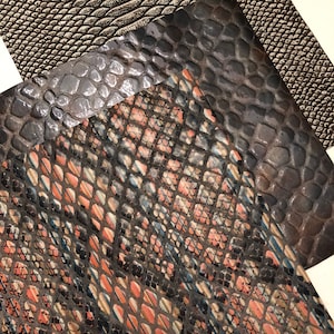 May include: Three different patterned faux snakeskin fabric swatches. The top swatch is a light brown with a subtle scale pattern. The middle swatch is a dark gray with a larger scale pattern. The bottom swatch is a black and brown with a more intricate scale pattern.