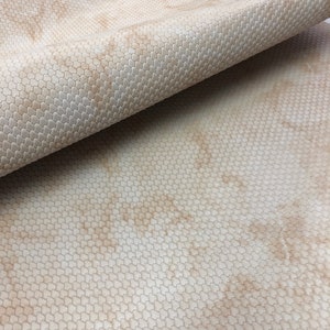 May include: A close-up of a beige textured fabric with a subtle pattern. The fabric has a slightly mottled appearance, with lighter and darker areas of beige.