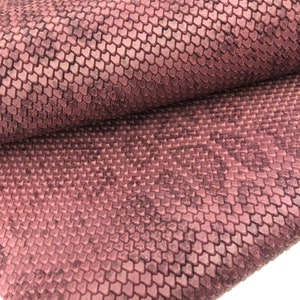 May include: A close-up of a textured fabric with a scale-like pattern in a deep burgundy color.