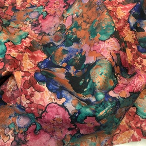May include: Abstract fabric with a colorful, marbled pattern in shades of pink, blue, green, and brown. The fabric has a textured, almost suede-like appearance.