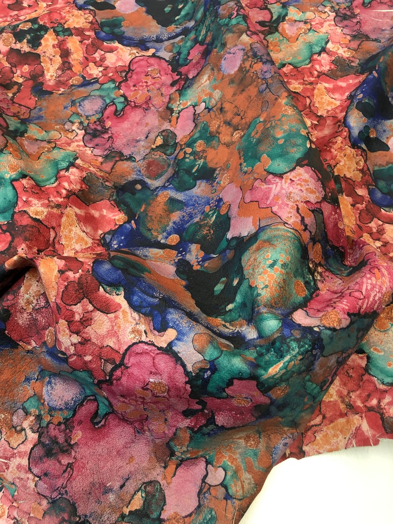 May include: Abstract fabric with a colorful, marbled pattern in shades of pink, blue, green, and brown. The fabric has a textured, almost suede-like appearance.