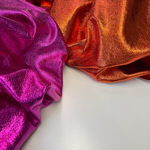 May include: Two pieces of metallic fabric, one in a bright pink and the other in a bright orange. The fabric has a textured surface and a shiny finish.