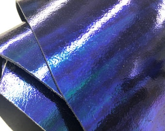 Op de afbeelding: Close-up van iriserend blauw leer met een subtiele groene glans. Het leer is dubbelgevouwen, waardoor het gladde, glanzende oppervlak zichtbaar is.