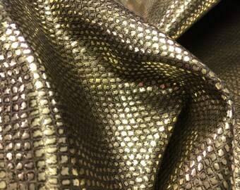 May include: Close-up of a gold metallic fabric with a snakeskin pattern. The fabric is textured and has a subtle sheen.