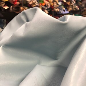 May include: A light blue leather hide with a textured surface. The leather is folded and draped over a surface.