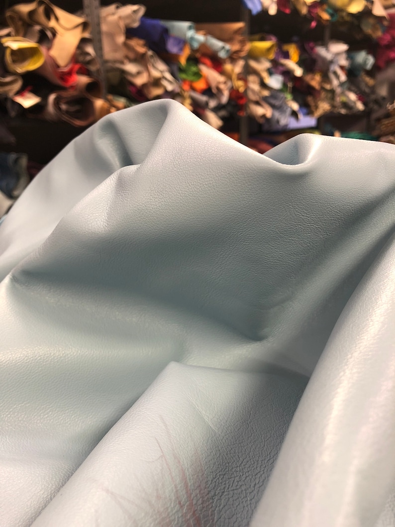 May include: A light blue leather hide with a textured surface. The leather is folded and draped over a surface.