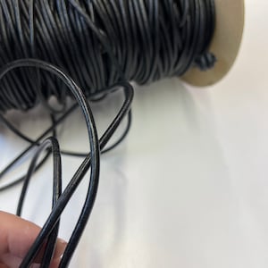 May include: A spool of black leather cord, with a length of cord unwound and held in a hand.