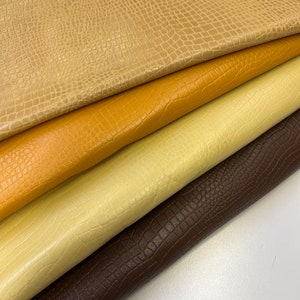 May include: Four pieces of faux leather fabric in different colors: brown, beige, yellow, and light beige. The fabric has a crocodile skin pattern.