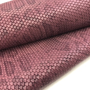 May include: A close-up of a textured, burgundy-colored fabric with a scale-like pattern. The fabric is folded in half, showing the texture and pattern on both sides.