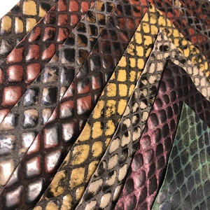 May include: Close-up of a variety of patterned leather strips in shades of brown, black, yellow, green, and purple. The strips are arranged in a diagonal pattern, creating a textured and visually appealing design.
