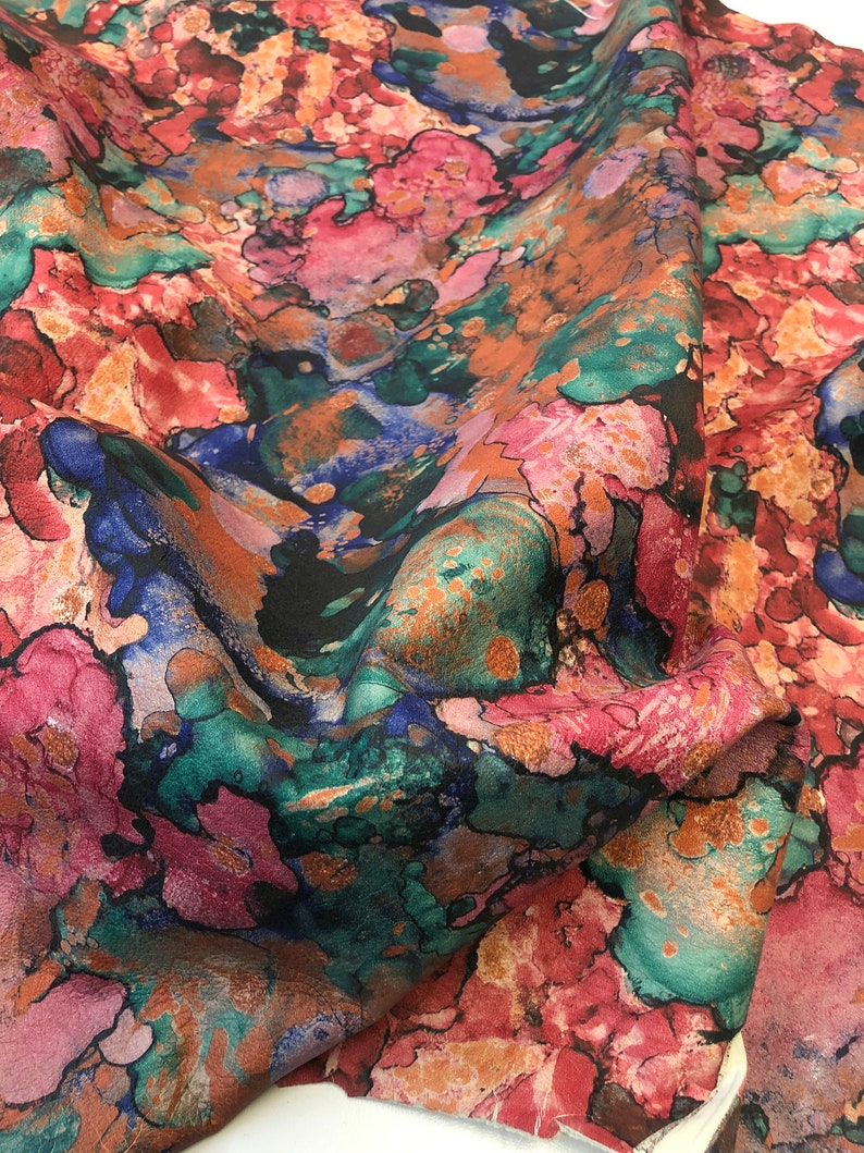 May include: Abstract fabric with a colorful watercolor-like pattern in shades of pink, blue, green, and brown.