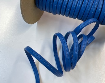 May include: A spool of blue leather cord with a stitched edge. The cord is wrapped around a cardboard spool.