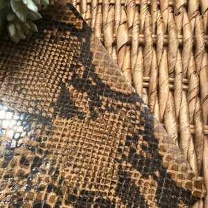 May include: Close-up of a brown and black snakeskin pattern fabric. The fabric has a glossy finish and a textured surface.