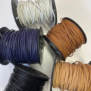 May include: Four spools of leather cord in different colors: white, navy blue, brown, and black. The cords are wound around black plastic spools.