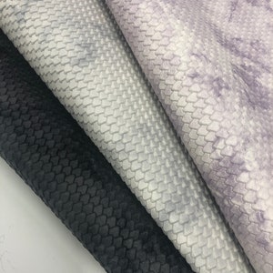 May include: Three fabric swatches with a textured, scale-like pattern. The swatches are in black, light gray with a purple tint, and white with a purple tint.