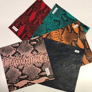 May include: Five different colors of faux snakeskin fabric swatches. The colors are fire red, teal, peach, blush pink, and navy blue.