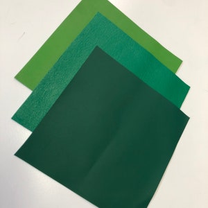 May include: Three squares of fabric in different shades of green. The top square is a light green, the middle square is a medium green, and the bottom square is a dark green.