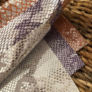 May include: Three sheets of faux snakeskin fabric in silver, purple, and orange. The fabric has a textured, embossed pattern.