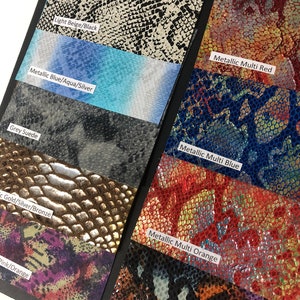 May include: A sample swatch book of different colored and patterned faux snakeskin fabrics. The swatches are labeled with their color and pattern names, including "Light Beige/Black", "Metallic Blue/Aqua/Silver", "Grey Suede", "Gold/Silver/Bronze", "Pink/Orange", "Metallic Multi Red", "Metallic Multi Blue", "Metallic Multi Orange", and "Blue/Purple/Orange/Black".