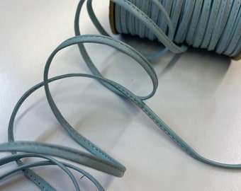 May include: A spool of light blue leather cord with a stitched edge. The cord is coiled and ready to be used for crafting projects.