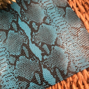 May include: A close-up of a blue and black snakeskin patterned fabric. The fabric has a textured surface and a glossy finish.