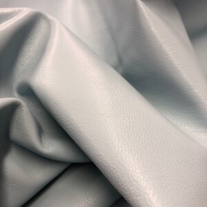 May include: Close-up of a light blue leather fabric with a textured surface.