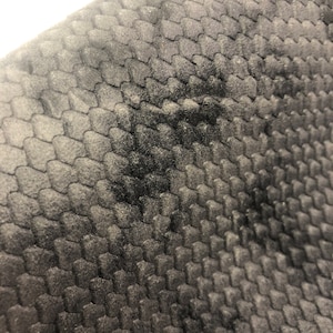 May include: Close-up of a black fabric with a textured, raised pattern resembling scales. The fabric has a soft, velvety feel.