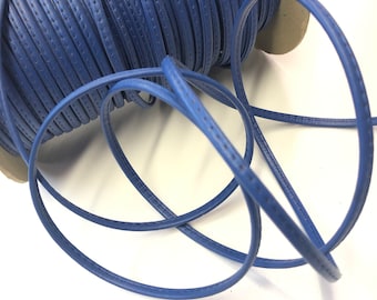 May include: A spool of blue leather cord with a stitched edge. The cord is wound around a cardboard spool.