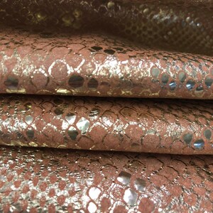 May include: Close-up of a folded piece of brown leather with a gold metallic snakeskin pattern.