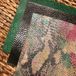 May include: Three different sheets of faux snakeskin fabric. The first sheet is a dark green, the second is black with a subtle shimmer, and the third is a light brown with a green, pink, and black pattern.