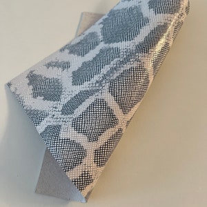 May include: White faux leather with a black snakeskin pattern. The leather is folded in half, showing the white backing.