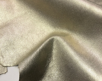 May include: A piece of metallic gold leather with a textured surface. The leather is folded and draped over a white surface.