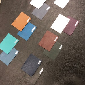 May include: A collection of 10 leather swatches in various colors, including teal, ocean blue, brown, dark blue, charcoal, forest green, burgundy, purple, gray, and white. The swatches are arranged on a black leather surface.