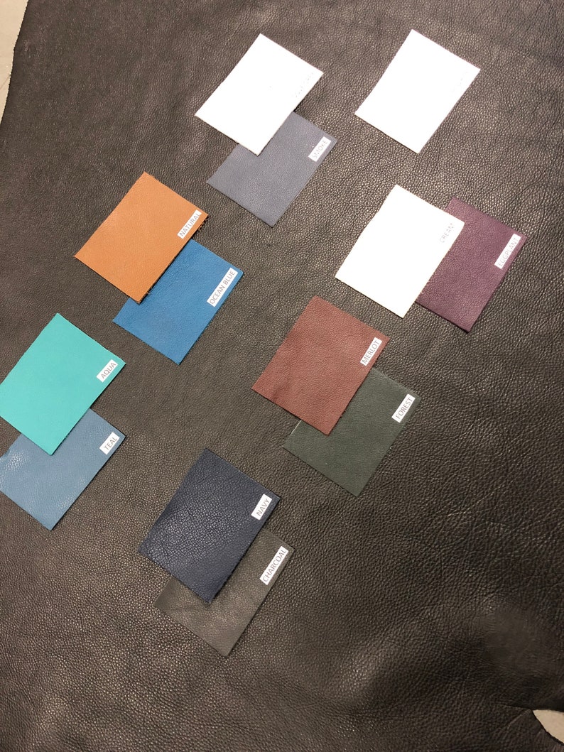 May include: A collection of 10 leather swatches in various colors, including teal, ocean blue, brown, dark blue, charcoal, forest green, burgundy, purple, gray, and white. The swatches are arranged on a black leather surface.